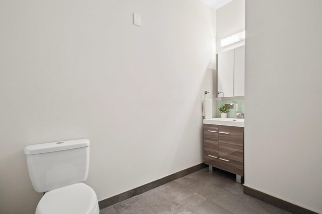 half bath with baseboards, toilet, and vanity