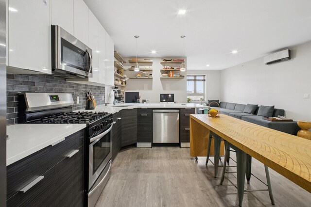 kitchen with appliances with stainless steel finishes, a wall mounted AC, open shelves, light wood-type flooring, and light countertops