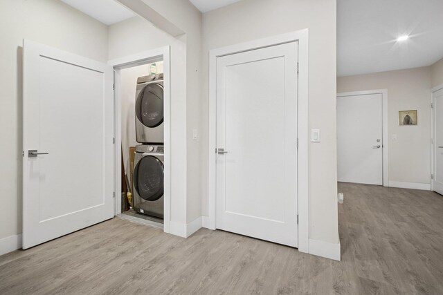 washroom with stacked washer and dryer, baseboards, light wood-style flooring, and laundry area