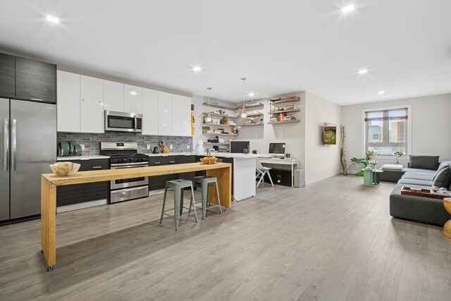 kitchen featuring open shelves, appliances with stainless steel finishes, light wood finished floors, light countertops, and open floor plan