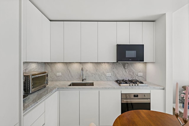 kitchen featuring stainless steel appliances, white cabinetry, a sink, and backsplash