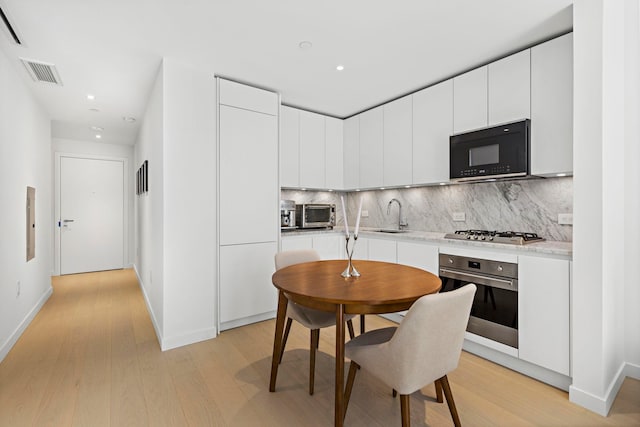 kitchen featuring stainless steel appliances, sink, white cabinetry, light hardwood / wood-style flooring, and decorative backsplash