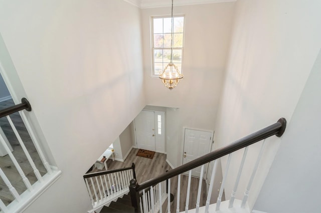 stairway with wood-type flooring, an inviting chandelier, and crown molding