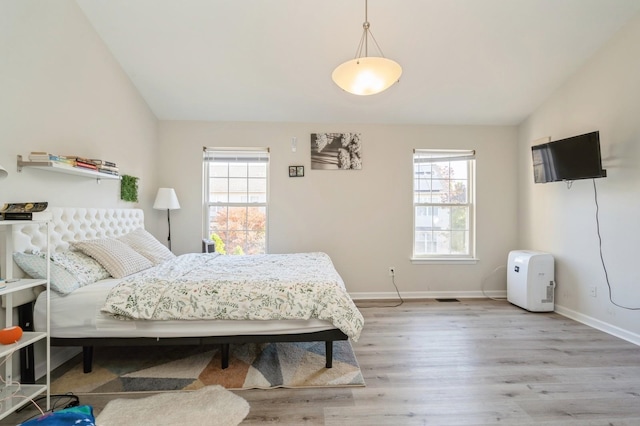 bedroom with light wood-type flooring, multiple windows, and vaulted ceiling