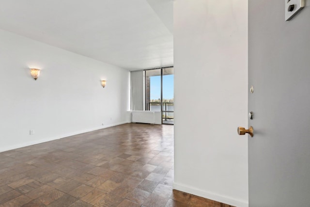 empty room featuring a wall of windows, baseboards, and a water view