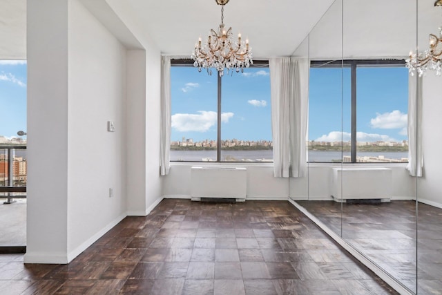 unfurnished dining area with a water view, baseboards, an inviting chandelier, and radiator heating unit