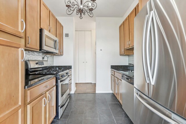 kitchen featuring appliances with stainless steel finishes, a sink, a chandelier, dark stone countertops, and visible vents
