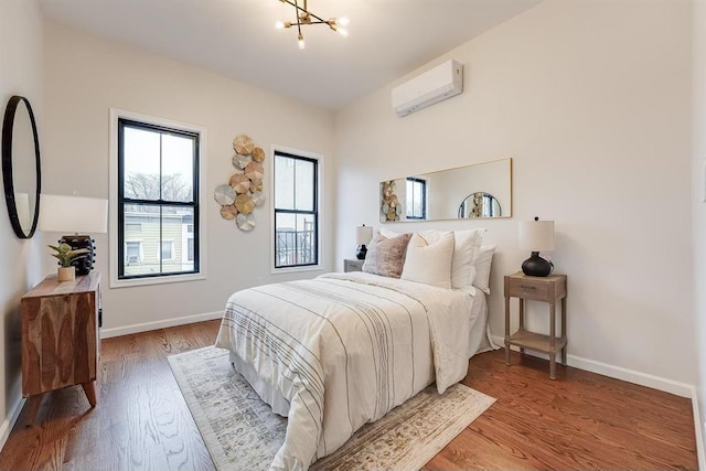 bedroom with a notable chandelier, a wall mounted air conditioner, and wood-type flooring