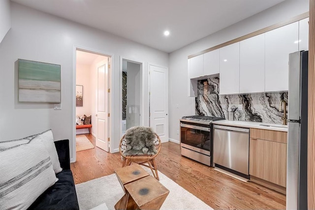 kitchen featuring stainless steel appliances, white cabinets, backsplash, and light hardwood / wood-style flooring