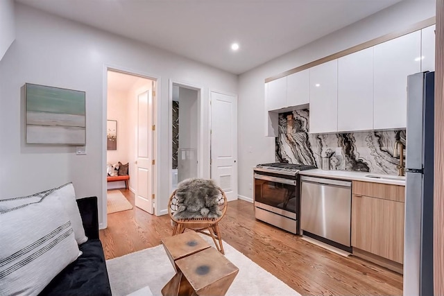 kitchen featuring appliances with stainless steel finishes, light wood-type flooring, light brown cabinets, white cabinetry, and tasteful backsplash