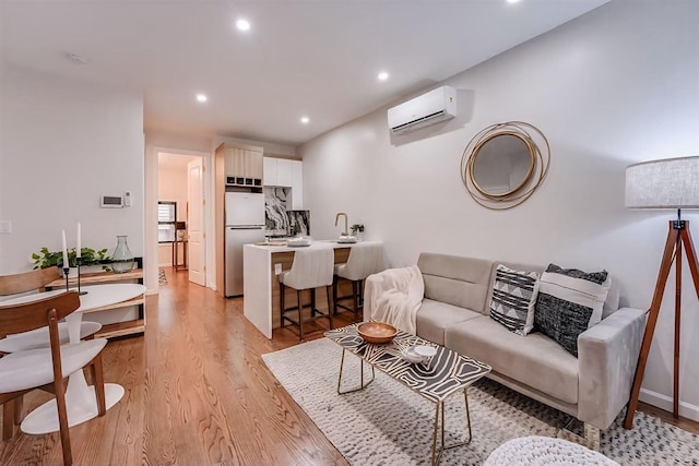 living room with sink, an AC wall unit, and light hardwood / wood-style floors