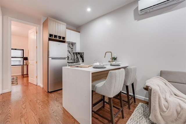 kitchen featuring kitchen peninsula, a breakfast bar, light wood-type flooring, stainless steel refrigerator, and a wall mounted air conditioner