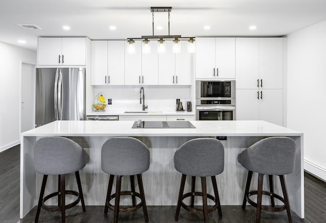 kitchen featuring sink, a kitchen bar, a center island with sink, white cabinets, and black appliances