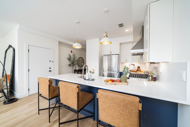 kitchen with visible vents, wall chimney range hood, appliances with stainless steel finishes, a peninsula, and a sink