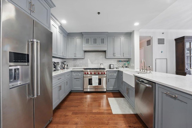 kitchen with high end appliances, gray cabinets, a sink, crown molding, and tasteful backsplash
