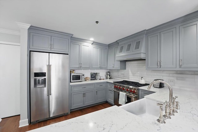 kitchen featuring premium appliances, gray cabinets, light stone countertops, a sink, and tasteful backsplash