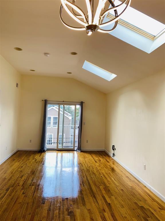 empty room with baseboards, vaulted ceiling with skylight, and wood finished floors