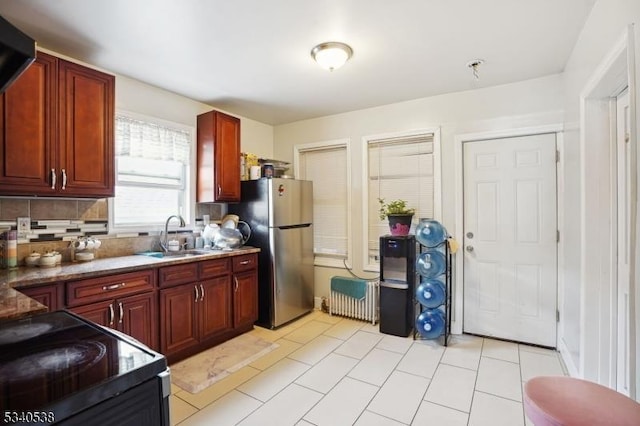 kitchen with black / electric stove, a sink, freestanding refrigerator, decorative backsplash, and reddish brown cabinets