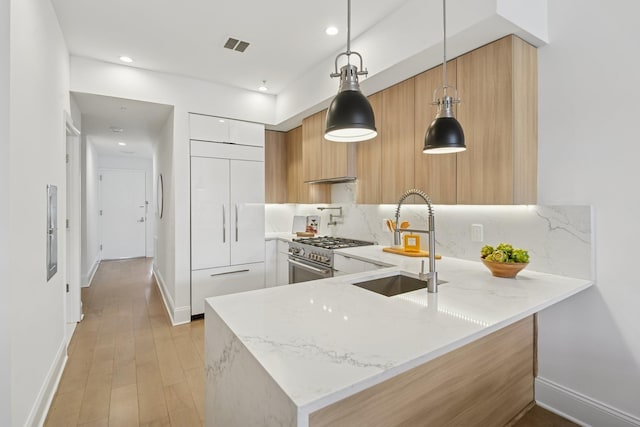 kitchen featuring a peninsula, high end appliances, a sink, and modern cabinets
