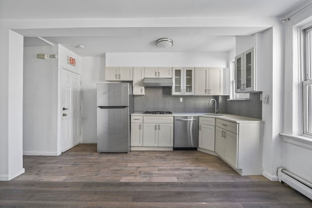 kitchen featuring glass insert cabinets, stainless steel appliances, light countertops, under cabinet range hood, and a baseboard heating unit