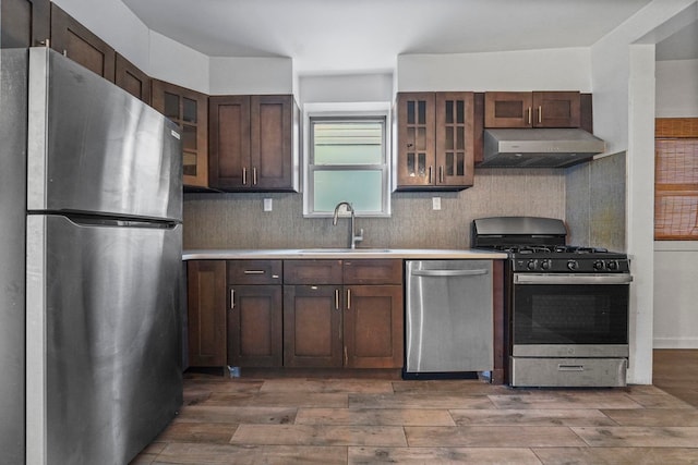 kitchen with glass insert cabinets, appliances with stainless steel finishes, light countertops, under cabinet range hood, and a sink