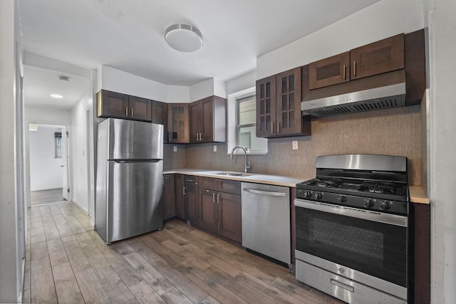 kitchen with stainless steel appliances, a sink, wood finished floors, light countertops, and glass insert cabinets