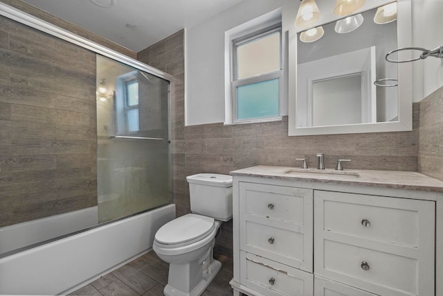 full bathroom featuring enclosed tub / shower combo, toilet, wood finished floors, vanity, and tile walls