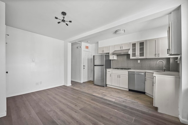 kitchen with decorative backsplash, glass insert cabinets, stainless steel appliances, light countertops, and under cabinet range hood