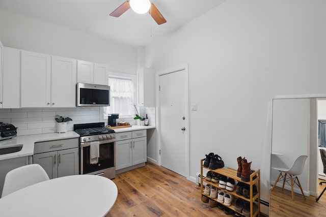 kitchen with light wood-style flooring, gray cabinetry, light countertops, appliances with stainless steel finishes, and decorative backsplash