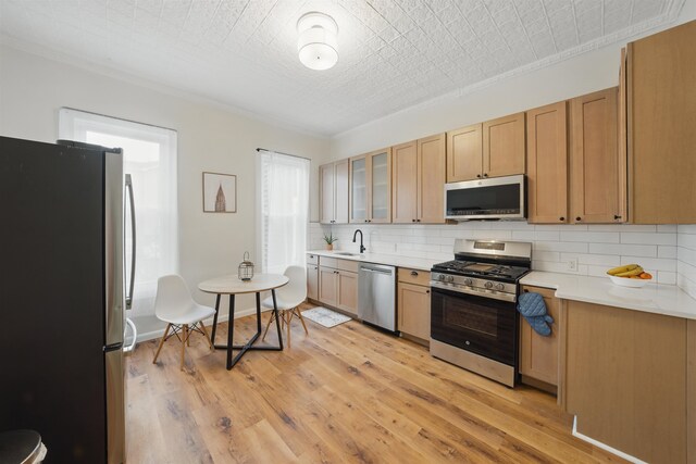 kitchen featuring tasteful backsplash, stainless steel appliances, light countertops, light wood-type flooring, and a sink