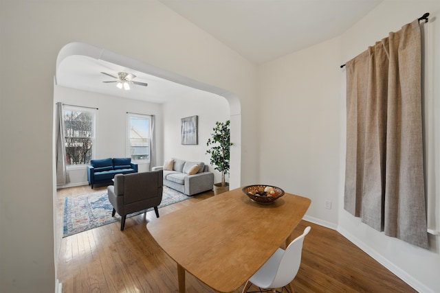 dining area featuring arched walkways, wood-type flooring, a ceiling fan, and baseboards