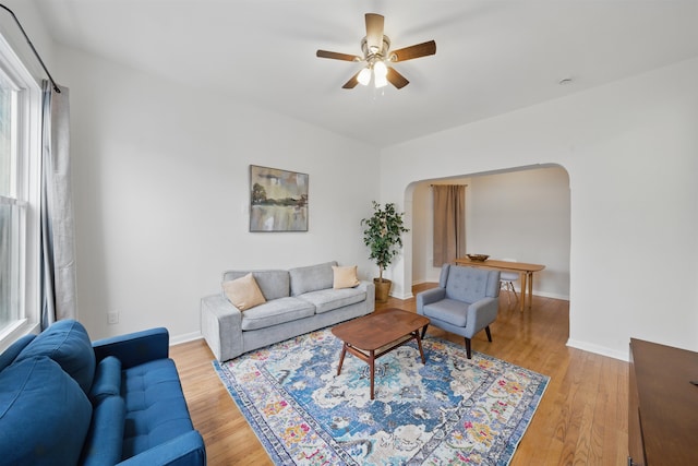 living room featuring light wood-type flooring, baseboards, and arched walkways