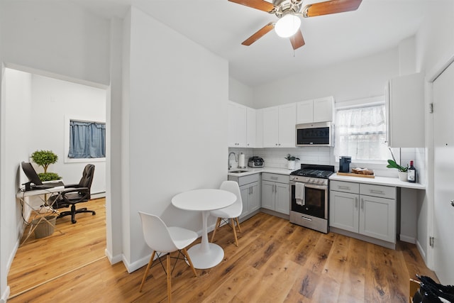 kitchen featuring light wood finished floors, light countertops, stainless steel appliances, gray cabinetry, and backsplash