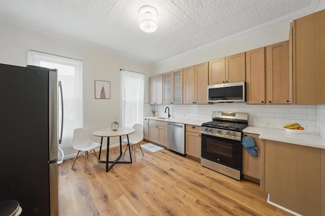 kitchen featuring backsplash, stainless steel appliances, light countertops, light wood-type flooring, and a sink