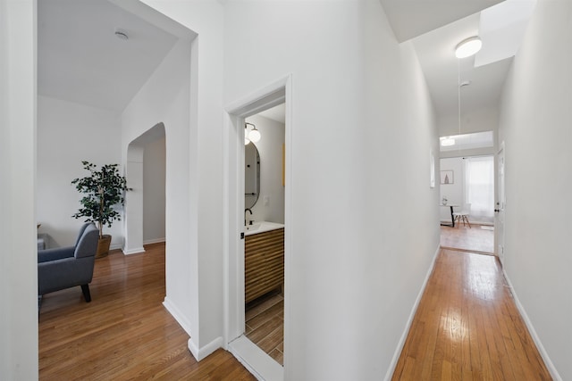 corridor with arched walkways, light wood-style flooring, and baseboards