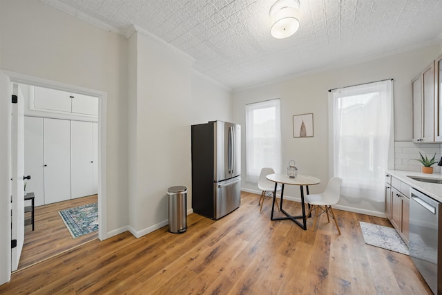 kitchen with baseboards, light wood-style floors, appliances with stainless steel finishes, tasteful backsplash, and crown molding