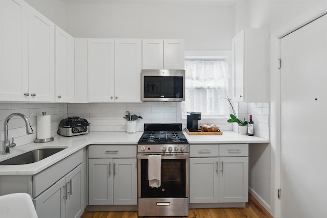 kitchen with tasteful backsplash, appliances with stainless steel finishes, light countertops, gray cabinetry, and a sink