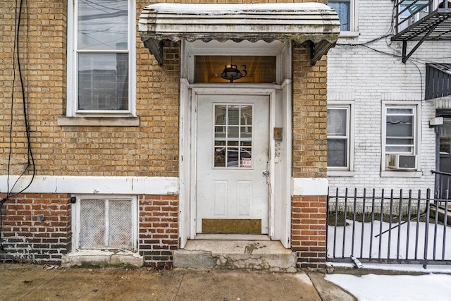 view of exterior entry featuring brick siding and fence