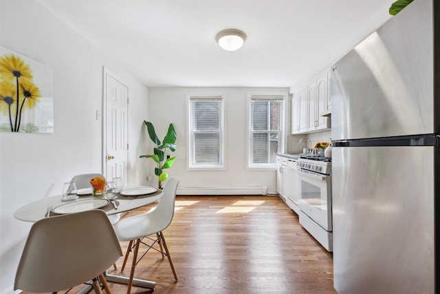 227 7th St, Jersey City, NJ 07302 - kitchen with freestanding refrigerator, wood finished floors, baseboard heating, white gas range, and white cabinets