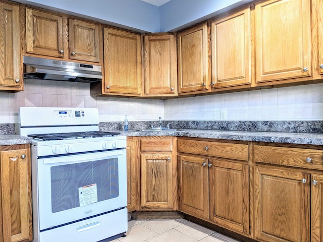 kitchen featuring sink, dark stone counters, decorative backsplash, white range with gas cooktop, and light tile patterned floors