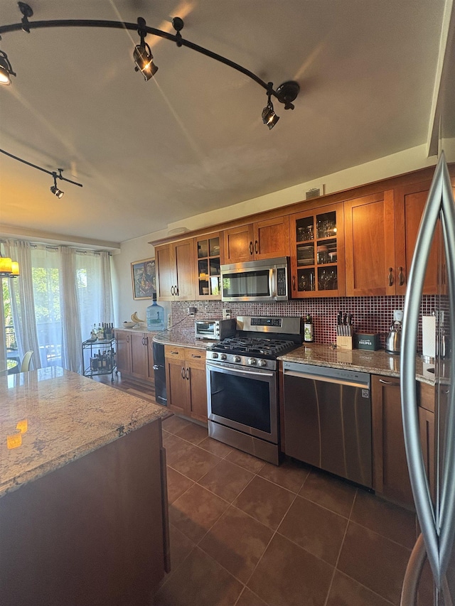 kitchen with stainless steel appliances, rail lighting, dark tile patterned floors, brown cabinets, and decorative backsplash