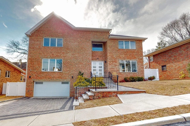 view of front facade with a garage, brick siding, decorative driveway, and fence