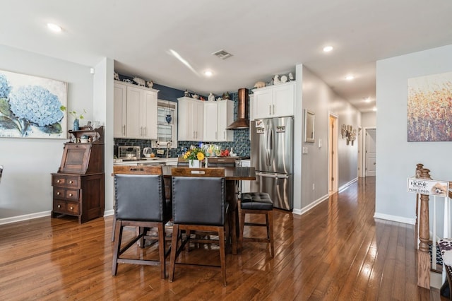 kitchen featuring wall chimney exhaust hood, a breakfast bar, white cabinetry, a center island, and stainless steel refrigerator