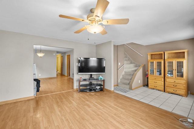 unfurnished living room featuring light wood-style floors, stairs, baseboards, and a ceiling fan