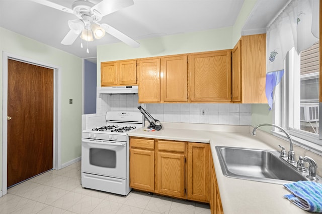 kitchen featuring tasteful backsplash, white range with gas stovetop, light countertops, under cabinet range hood, and a sink