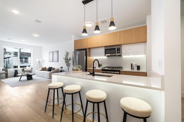 kitchen with a kitchen bar, sink, decorative light fixtures, light wood-type flooring, and stainless steel appliances