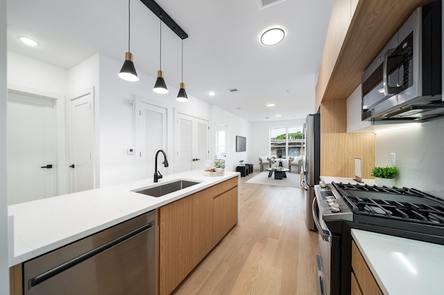 kitchen with sink, hanging light fixtures, light stone counters, light hardwood / wood-style floors, and stainless steel appliances