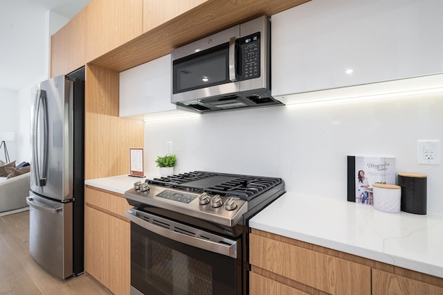 kitchen featuring light stone countertops, stainless steel appliances, and light wood-type flooring