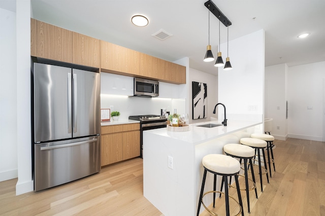 kitchen featuring a breakfast bar, sink, a center island with sink, pendant lighting, and stainless steel appliances