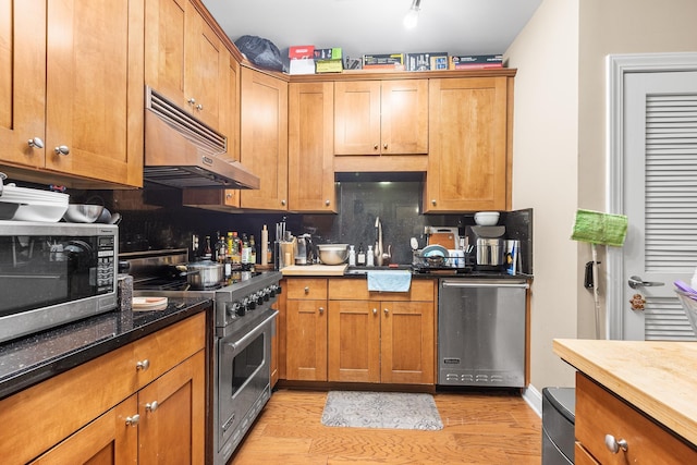 kitchen featuring under cabinet range hood, a sink, stainless steel appliances, light wood-style floors, and brown cabinetry